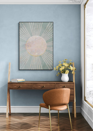 Framed Sage Green Boho Sun Rays wall art above a wooden desk with flowers, in a modern room setting.