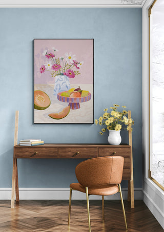 Wall art of a colorful fruit still life, titled "Fruit Break - Goed Blauw," hanging above a wooden desk.