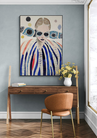 Deep Breath by Martin Zen hangs above a wooden desk with a vase of yellow flowers and an orange chair.