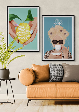 Two framed art prints above a tan sofa, including "Might Be Wine - ByKammille" on a blue background.