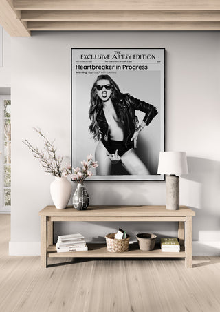 Framed "Heartbreaker in Progress Artsy Edition" poster above a wooden table with decor in a modern room.