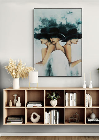 Framed Three Hats artwork by David Wolf hanging above a wooden shelf with decor and books.