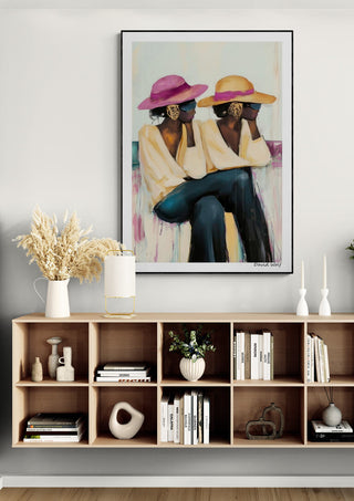 Framed "Break" by David Wolf featuring two women with hats, displayed above a modern shelf with decor.