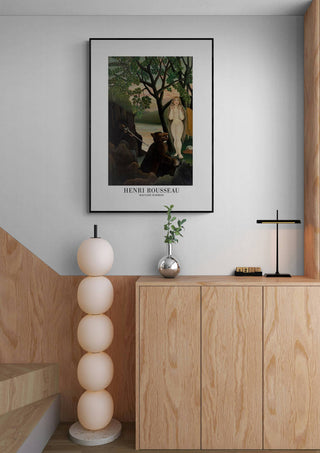 Framed Mauvaise Surprise by Henri Rousseau hanging above a wooden cabinet in a modern interior setting.
