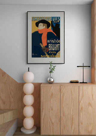 Framed "Aristide Bruant Dans Son Cabaret" Lautrec poster hanging above a wooden cabinet in a modern room.