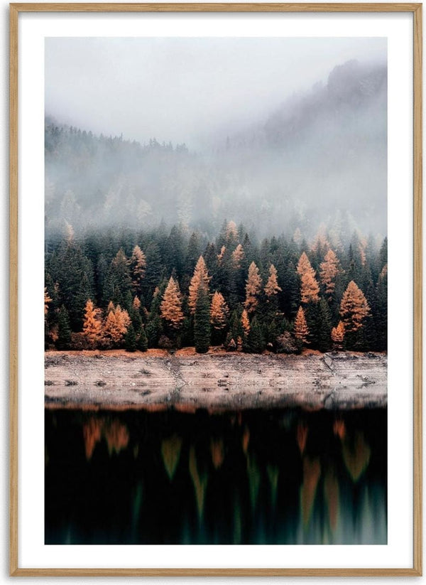 Autumn trees with orange foliage reflected on a calm lake, misty forest and mountains in the background.