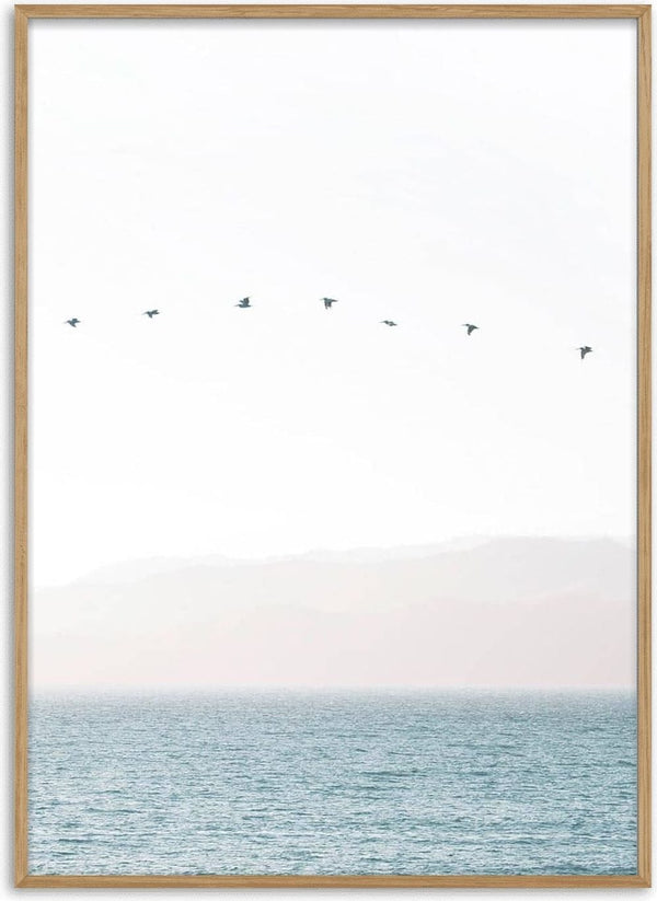 Minimalist artwork of birds flying in a straight line over calm water with soft mountains in the background.