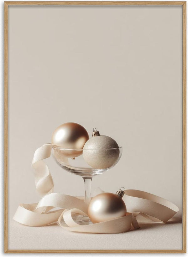 Three elegant glass Christmas balls and a cream ribbon displayed in and around a glass on a neutral background.