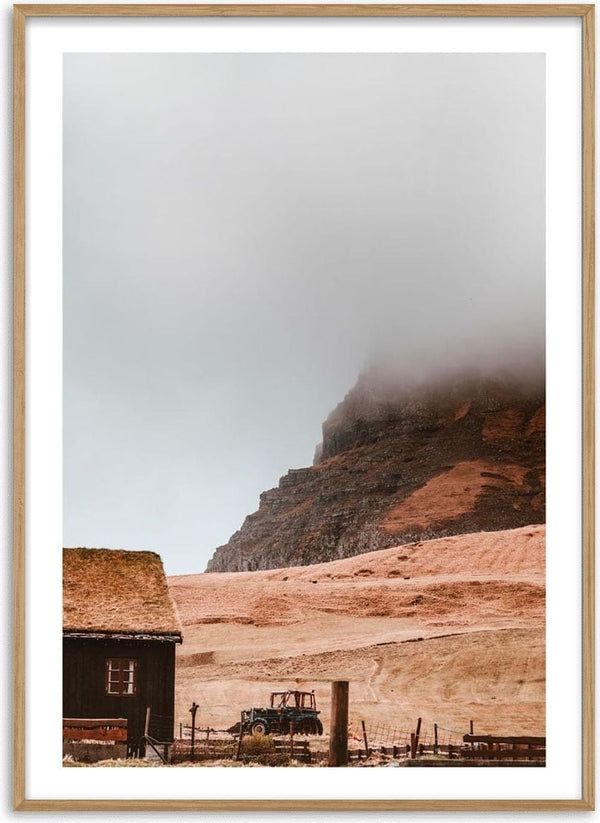 A misty mountain rises behind a rustic field and wooden building, featured on the Cloudy Mountain Plakat product page.