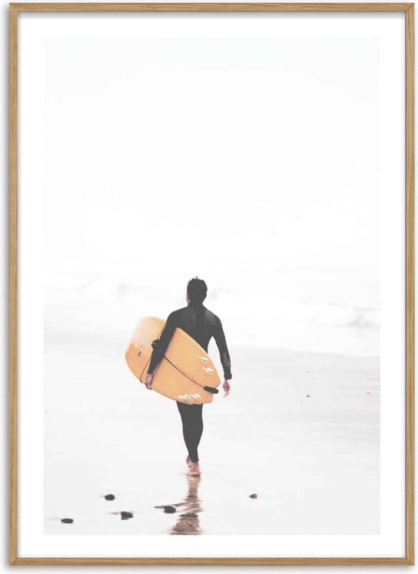A surfer in a wetsuit walks on the beach carrying a yellow surfboard toward the ocean.