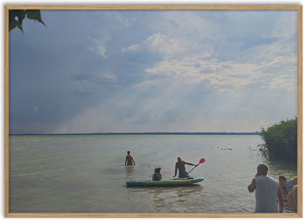 The Lake’s Shared Rhythm by Bora Kőhalmi - swimmers and a paddleboarder on the green water of Lake Balaton under a wide cloudy sky