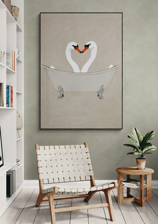 Framed art print of two swans forming a heart shape in a bathtub, displayed above a chair and plant.