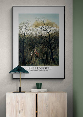 Framed print of "Rendezvous In The Forest" by Henri Rousseau hanging above a light wood cabinet.